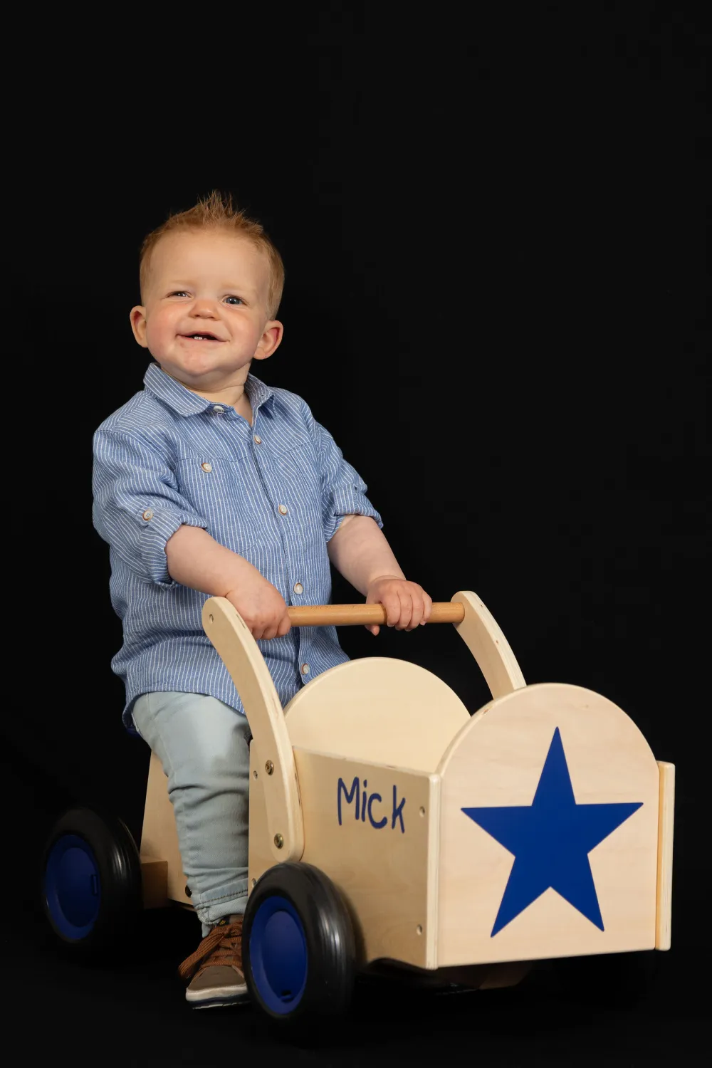 Lachende peuter met een houten loopwagen in de studio
